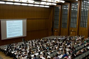 Picture: A full lecture hall at the University of Cologne. All students are listening to a presentation. 