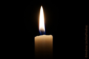 A burning candle in front of a dark background